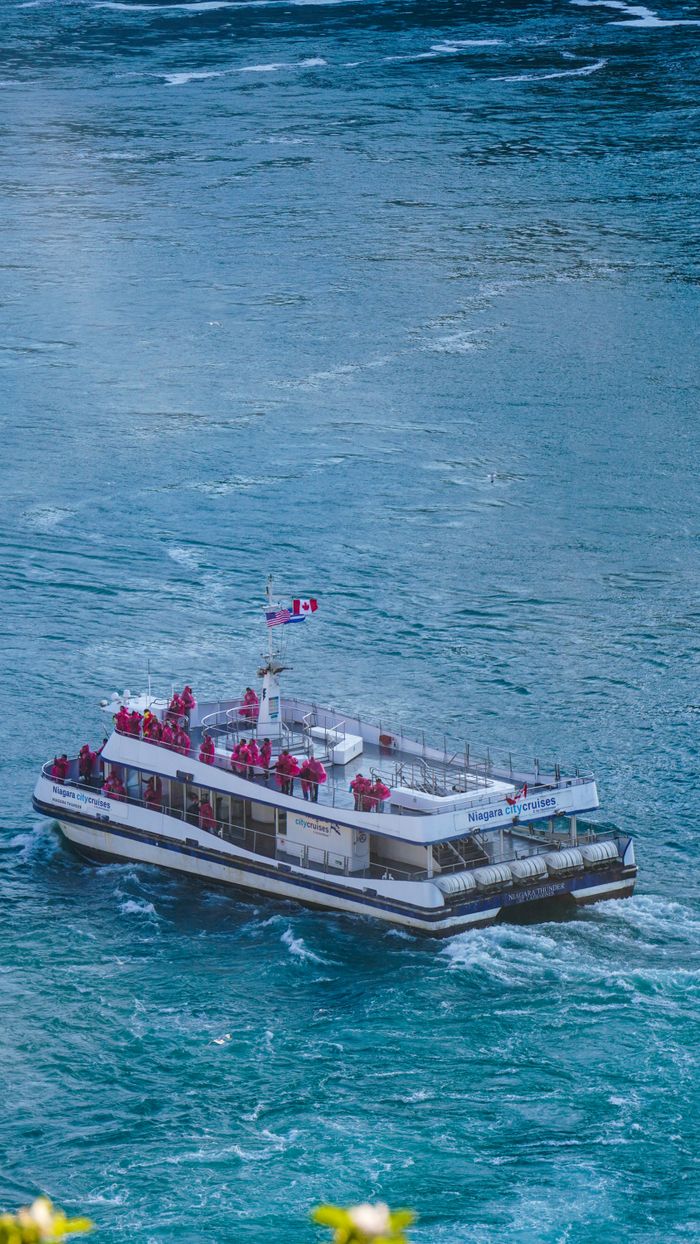 Aerial view of a tourist boat with people in red coats cruising Niagara River near Niagara Falls, Canada.