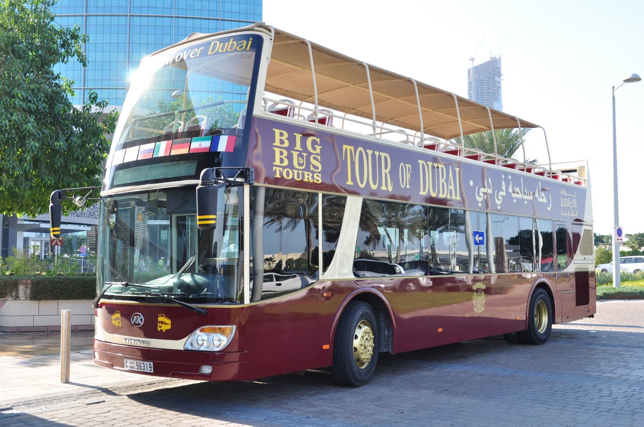 An open-top tour bus parked in Dubai, offering a city sightseeing tour under the sunny skies.