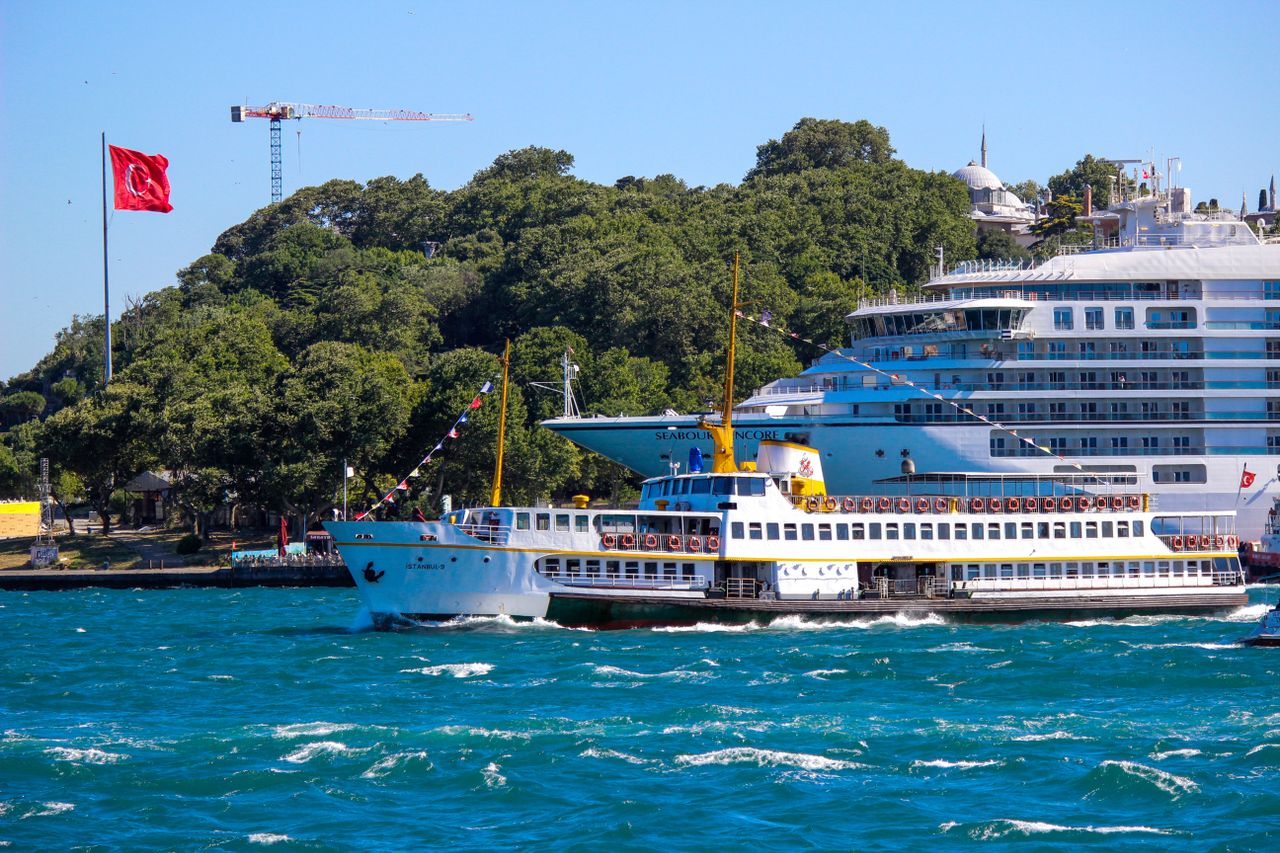 Cruise ship and ferry navigating near Istanbul with Turkish flag and scenic backdrop.